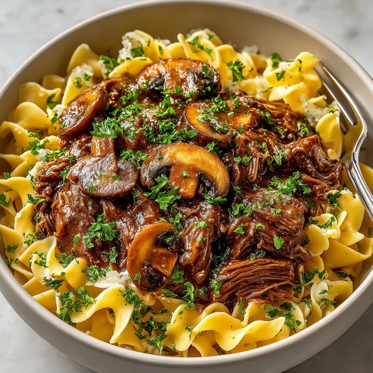 Slow cooker Beef & Mushroom Gravy simmers, ready over a heap of tender egg noodles.
