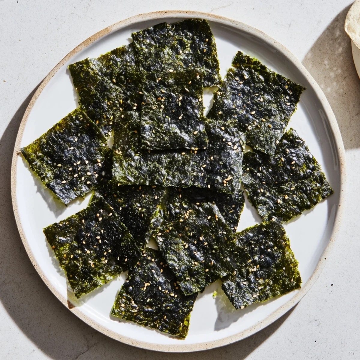 Golden-baked roasted seaweed chips on a dark plate, showing crispy layered nori sheets with salt crystals glistening for a savory snack.