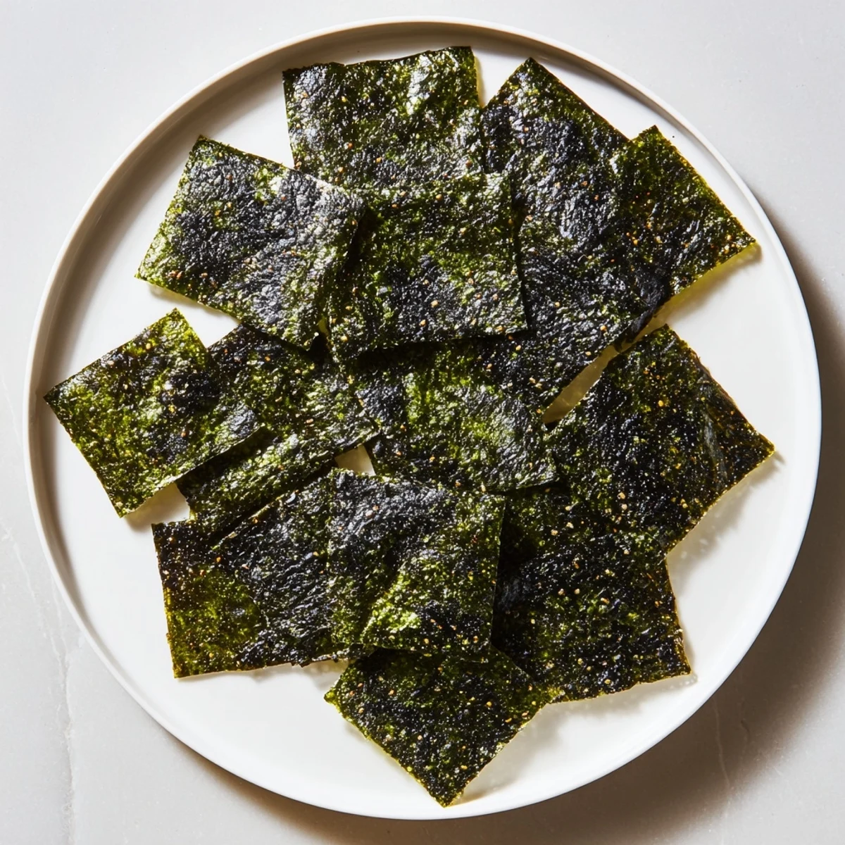 Homemade roasted seaweed chips arranged on parchment with sesame oil brushed layers, offering a crunchy, light bite ideal for vegan snacking.