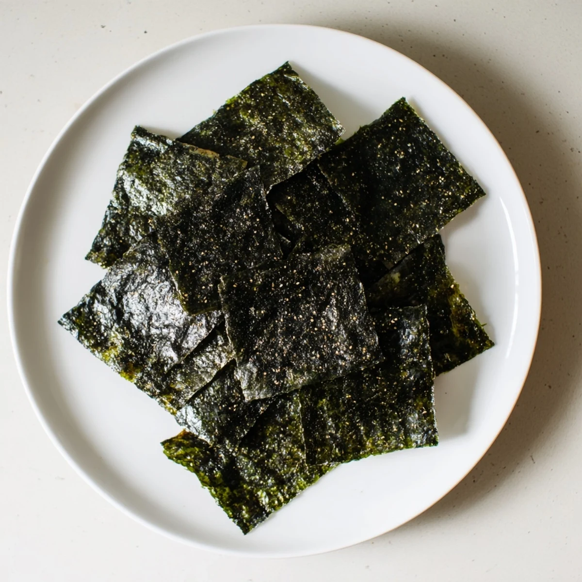Close-up of crispy roasted seaweed chips with dark green color, scattered salt flecks and a pinch of chili flakes for heat.