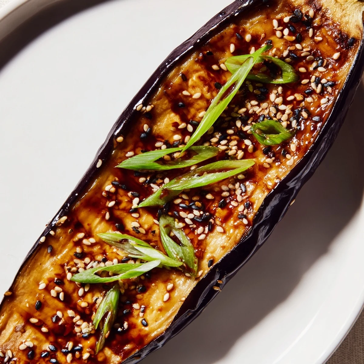 Golden roasted Miso Glazed Eggplant halves glisten with a sweet-savory glaze, sprinkled with sesame seeds and green onions.  