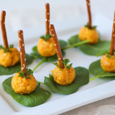 Colorful "Pumpkin Patch" grid appetizer, showcasing vibrant orange cheese ball pumpkins with pretzel stems.