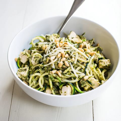 A close-up of Pesto Zucchini Chicken Bowl garnished with grated Parmesan and toasted pine nuts.