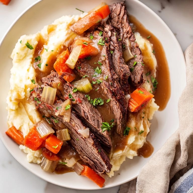A close-up of a richly flavored Slow Cooker Pot Roast, perfectly cooked, atop fluffy mashed potatoes.