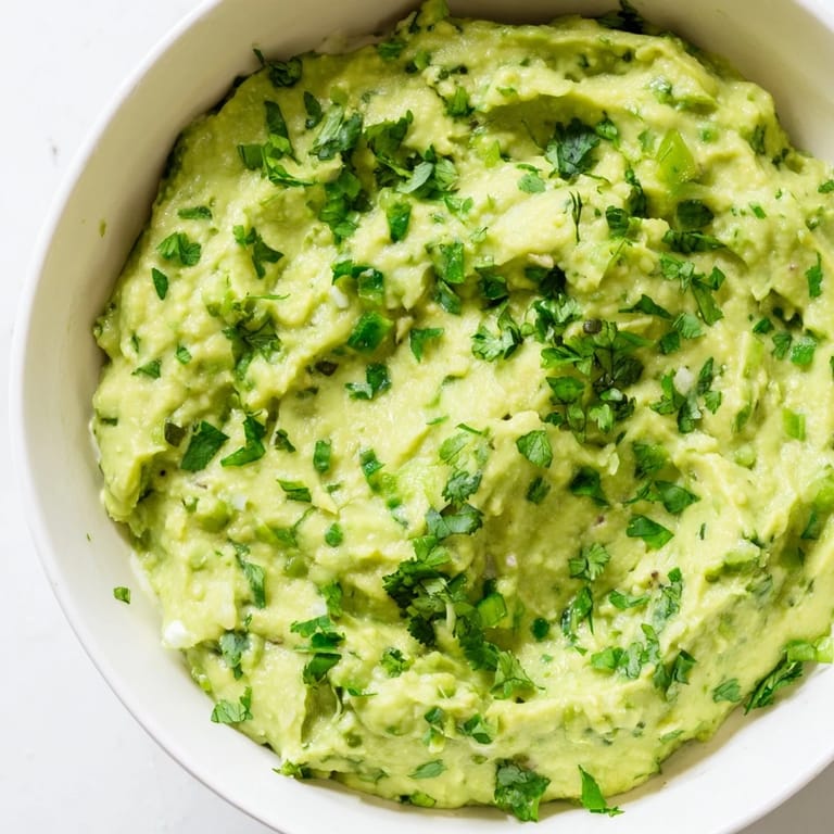 Zesty avocado lime dip in a serving bowl with a tortilla chip dipped into its chunky texture.