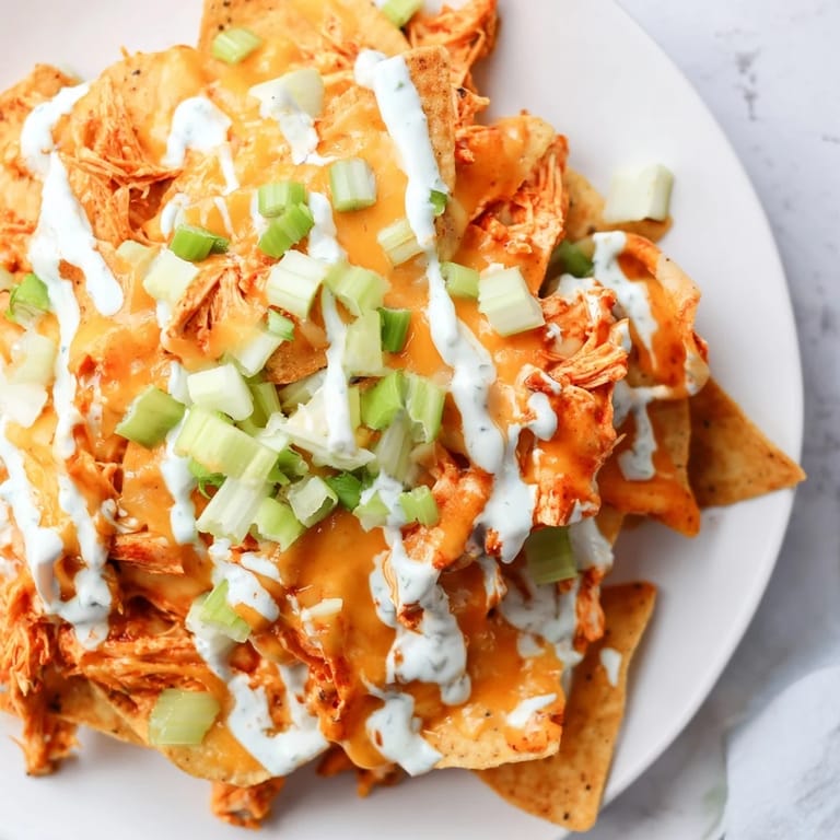 Fresh green onions and cool ranch drizzle top these baked Buffalo Chicken Nachos on a serving platter.